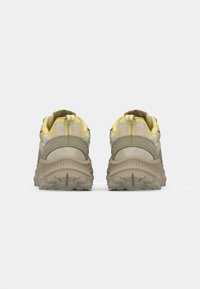 Beige and light yellow athletic shoes with a textured upper, detailed stitching, and a rugged rubber sole, viewed from the back.