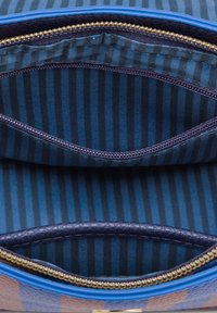 Blauwe ritszak interieur met blauw en marineblauw gestreepte voering. Twee compartimenten met gladde textuur en gouden ritsdetails.