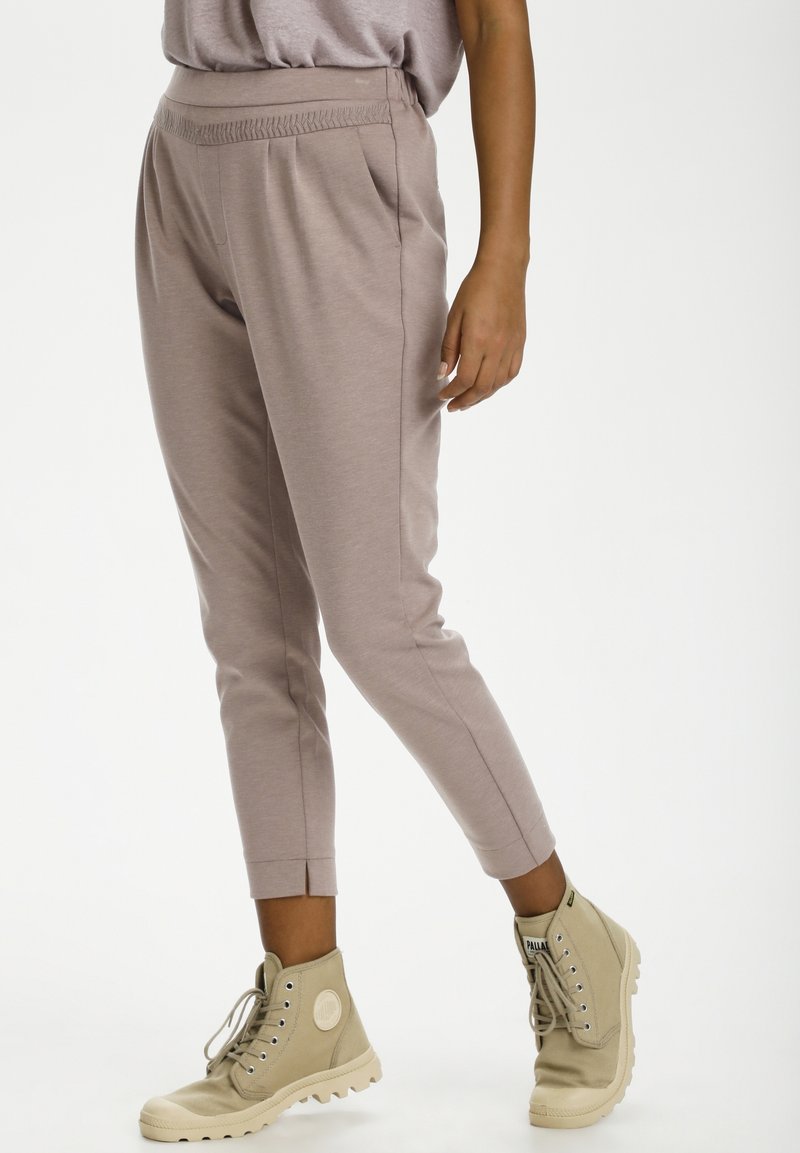 Helle taupefarbene, tapered Hosen mit texturiertem Bund und seitlichen Taschen, kombiniert mit beigen Knöchelschuhen mit dicker Sohle.