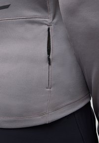 Giacca zip grigia chiara con tessuto texture, design a coste e cuciture piatte. Tasca con zip sul lato sinistro vicino all'orlo.
