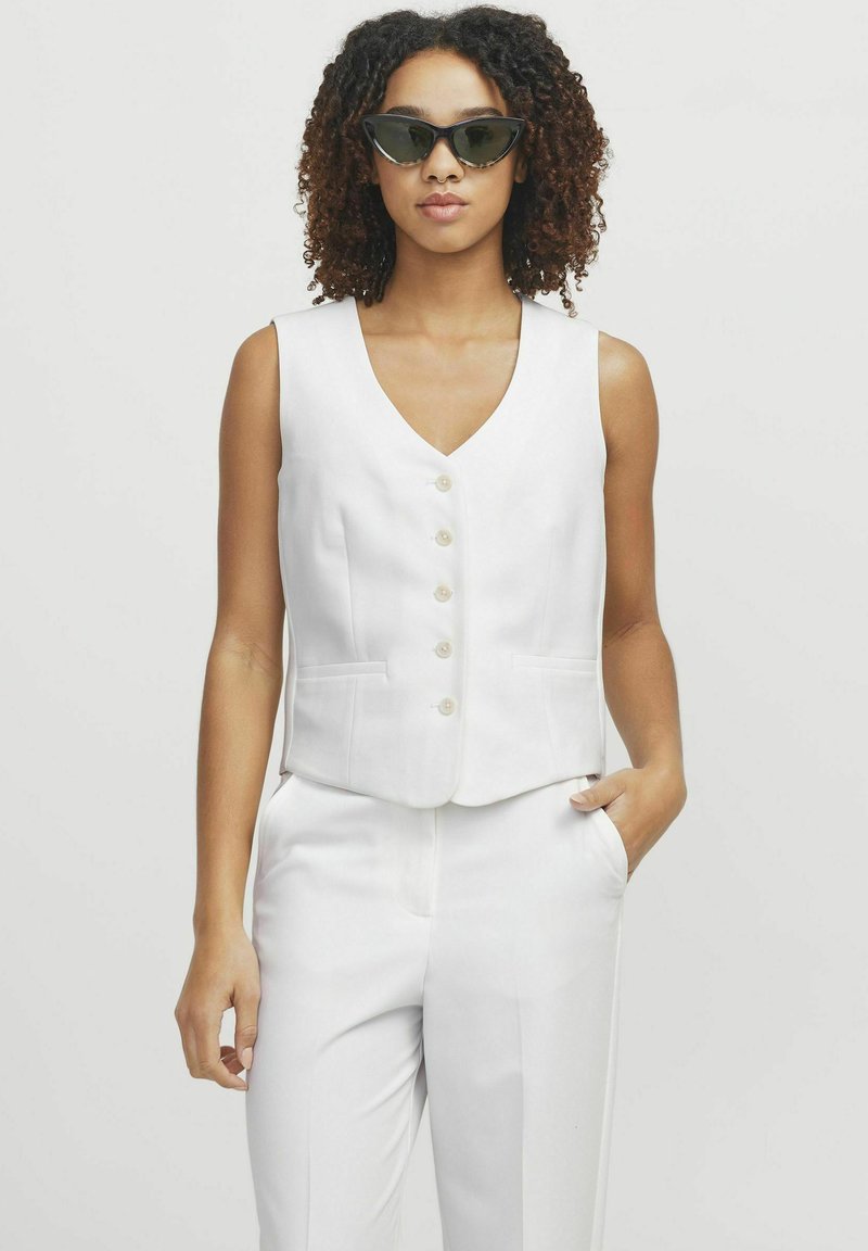 Biała bezrękawnik o dekolcie w kształcie litery V i pięcioma guzikami, z dwoma bocznymi kieszeniami i dopasowanym krojem. Połączony z pasującymi spodniami.