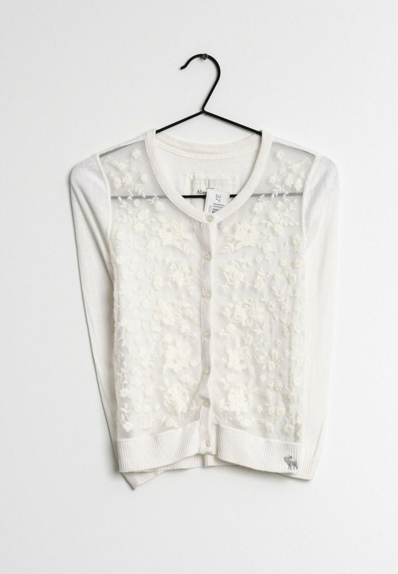 Cardigan bianco con ricami floreali trasparenti sul davanti, polsini e orlo a costine, e un piccolo accento del logo vicino al fondo.