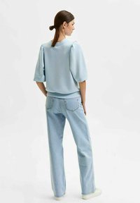 Light blue pullover with puff sleeves, rounded neckline, paired with light blue straight-leg denim jeans. Smooth texture, minimal detailing.