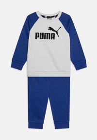 Puma dviejų dalių treningas šviesiai pilkos ir mėlynos spalvos. Yra apvalus kaklas, ilgos rankovės ir kelnės su elastingais rankogaliais. Ryškus logotipas ant viršaus.