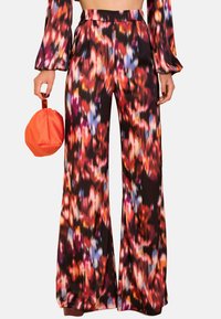 Pantalones de pierna ancha negros que presentan un colorido patrón abstracto floral en rojo, azul y naranja. Acompañados de un bolso redondo naranja.