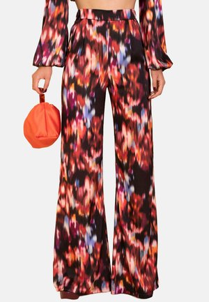 Pantalones de pierna ancha negros que presentan un colorido patrón abstracto floral en rojo, azul y naranja. Acompañados de un bolso redondo naranja.