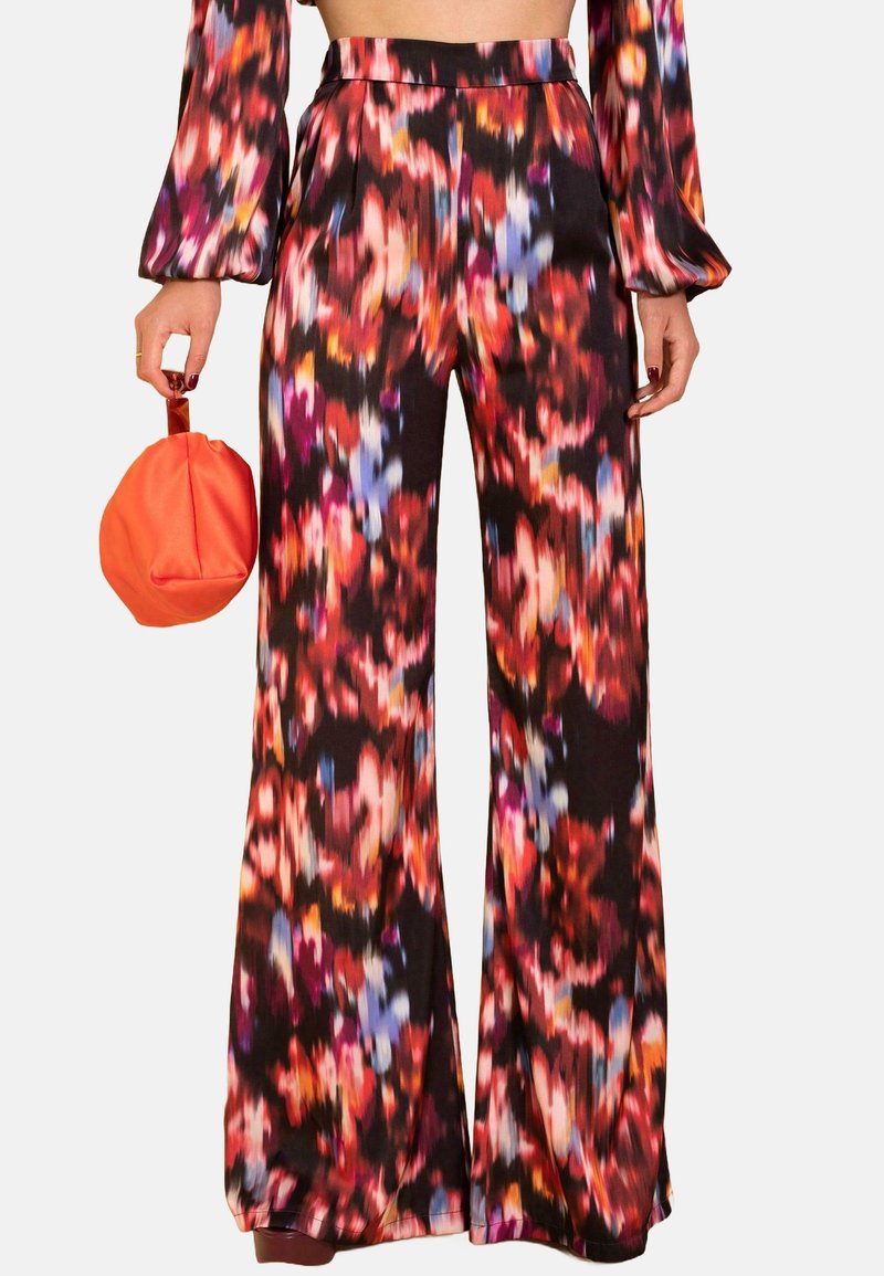 Pantalones de pierna ancha negros que presentan un colorido patrón abstracto floral en rojo, azul y naranja. Acompañados de un bolso redondo naranja.