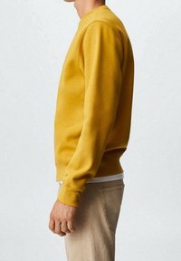Gelbes Crewneck-Sweatshirt aus weichem Stoff, mit langen Ärmeln, gerippten Bündchen und einem lässigen Schnitt, kombiniert mit hellbeigen Hosen.