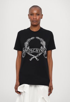 Melna kokvilnas T-kreksa ar baltu grafisko dizainu, kurā attēloti lauru zaru motīvi un vārds "MOSCHINO" lentē, īsas piedurknes un brīvs piegriezums.