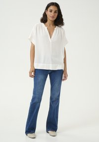 White, lightweight blouse with a v-neck and short sleeves, paired with blue flared jeans and beige slip-on shoes. Simple and clean design.