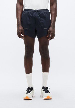 Marineblå atletiske shorts med teksturert stoff, elastisk midjebånd og sidelommer. Kombinert med hvite sokker og lette joggesko.