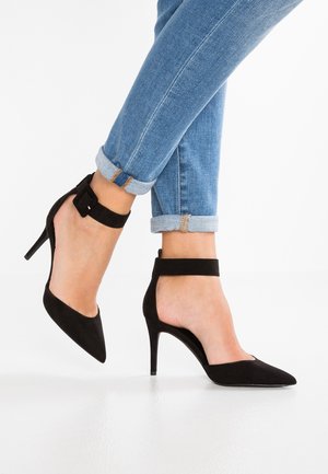 Black suede high-heeled shoes with a pointed toe and ankle strap, featuring a cut-out design and a slim stiletto heel.