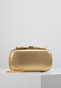 Zlatá metalická clutch kabelka s hladkým povrchem, obdélníkovým tvarem, mašlí na vrchu a odnímatelným řetízkovým popruhem.