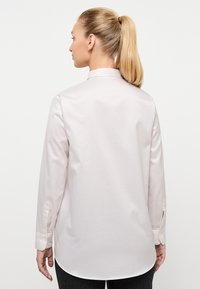 Camicia a maniche lunghe rosa chiaro con colletto, orlo arrotondato e polsini con bottoni. Tessuto morbido con un design minimale.