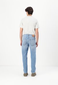Light blue denim jeans with a straight-leg fit, back pockets, and a branded leather patch on the waistband, paired with a gray t-shirt.