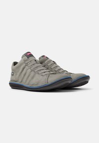 Scarpe da ginnastica grigie con un design strutturato, dotate di una suola nera e accenti blu. I lacci sono allacciati, evidenziando uno stile moderno e informale.