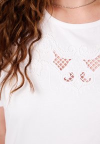 Witte top met ingewikkelde tonale borduursels en uitsnijdingen bij de halslijn, met een zachte textuur en korte mouwen.