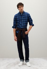 Blue plaid button-up shirt with long sleeves, paired with dark denim jeans and white sneakers. Brown textured knit tied around the waist.