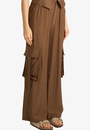 Pantaloni marroni a gamba larga con grandi tasche cargo laterali e cinturini regolabili, abbinati a sandali beige con punta aperta e fibbie.