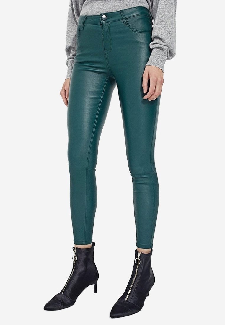 Femme portant un pantalon slim en cuir bleu sarcelle taille haute, un haut gris à manches longues et des bottines noires avec fermeture éclair à l'avant et petits talons.
