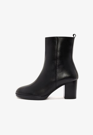Bottine en cuir noir avec une texture lisse, bout rond et talon carré. Dispose d'une languette à l'arrière pour un enfilage facile.