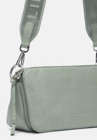 Grüne Leder-Crossbody-Tasche mit glatter Textur, ausgestattet mit einem silbernen Hardware-Gurt und geprägtem Branding auf der Vorderseite.