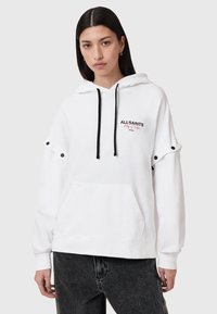 Sudadera blanca con un bolsillo frontal, cordones negros y logotipo bordado "ALL SAINTS". Presenta detalles de snaps en las mangas y puños acanalados.