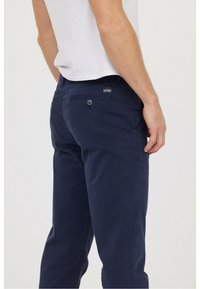 Chinos bleu marine avec une texture lisse, dotés d'une poche arrière avec un bouton et d'un petit label logo au-dessus de la poche.