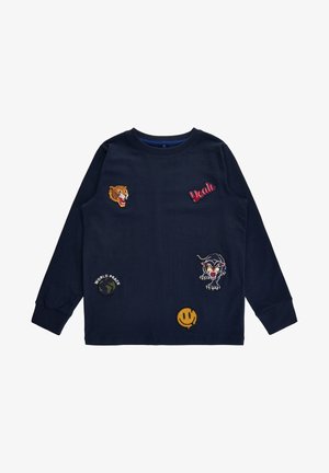 Marineblaues Langarmhemd mit Aufnähern, darunter ein brüllender Tiger, der Schriftzug "Yeah", ein schwarzer Panther, ein Smiley-Gesicht und eine Weltkugel mit der Aufschrift "World Peace".