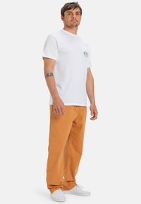 Hvit bomulls t-skjorte med en liten oransje og blå logo, kombinert med oransje bukser og hvite joggesko, minimalistisk design, avslappet passform.