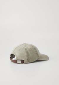 Cappello in cotone beige con visiera curva, tessuto testurizzato e una cinturino regolabile marrone sul retro con una fibbia in metallo argentato.