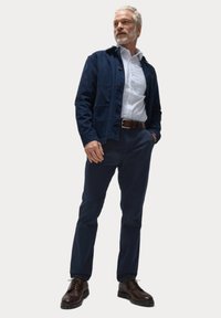 Giacca in cotone blu navy sopra una camicia bianca, abbinata a pantaloni blu scuro e scarpe in pelle marroni. Presenta una vestibilità comoda e dettagli con bottoni.
