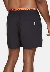 Schwarze Badeshorts aus strukturiertem Stoff mit einem elastischen Bund und einem orangefarbenen "JACK & JONES"-Logo; eine hintere Tasche.