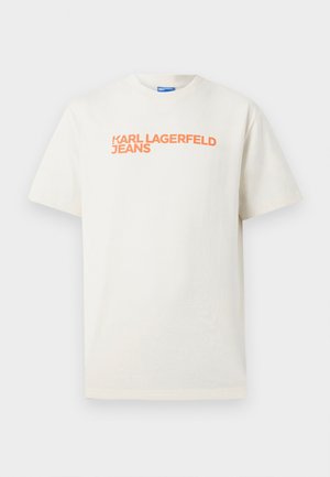 Hvit T-skjorte med korte ermer og oransje teksten "KARL LAGERFELD JEANS" trykt over brystet, forfra mot nøytral bakgrunn.