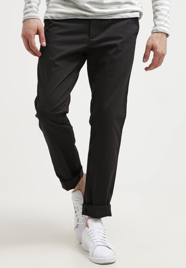 Black cotton pants with a straight cut, featuring rolled cuffs. Paired with white sneakers and a gray striped long-sleeve shirt.
