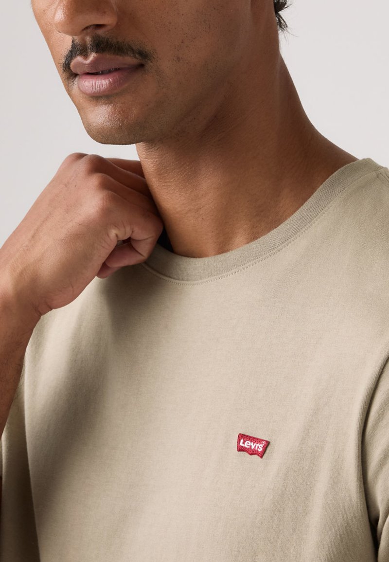 Beige bomulls-t-shirt med rund halsringning och korta ärmar, med en liten röd Levi's-logotyp på vänster bröst.