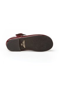 Zapato burdeos con un acabado de charol brillante, suela de goma negra texturizada y ornamento decorativo. Talla marcada como 22, fabricado en España.
