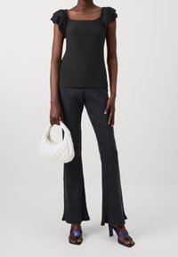 Černý top s čtvercovým dekoltem a volánkovými rukávy, kombinovaný s tmavými žebrovanými kalhotami s rozšířenými nohavicemi. Bílá prošívaná kabelka a fialové sandály na podpatku.