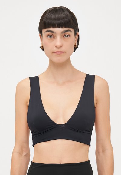 Brassière sans fil noire avec un décolleté en V profond et de larges bretelles, fabriquée en tissu lisse, dotée d'un design court et de coutures minimales.
