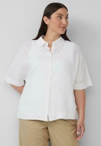 Witte, kortekraag linnen overhemd met knoopsluiting en een klassieke kraag. De stof heeft een lichte, gestructureerde afwerking. Gecombineerd met beige broeken.