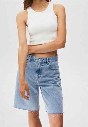 Top corto blanco de canalé combinado con pantalones cortos de mezclilla azul claro. Los pantalones cortos tienen un ajuste holgado, dobladillo deshilachado y diseño clásico de 5 bolsillos.