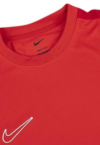 Czerwona sportowa koszulka Nike z okrągłym dekoltem, wykonana z lekkiego materiału, z małym białym logo na lewej stronie klatki piersiowej.