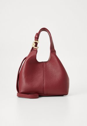 Burgundy leather handbag with textured finish, curved shape, short handle, and gold-tone hardware detail. Adjustable shoulder strap included.