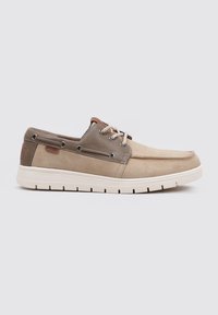 Zapatos de barco beige con un superior de ante suave, detalles en cuero marrón, ojales de metal y una suela de goma blanca con diseño antideslizante.