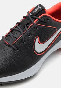 Μαύρο αθλητικό παπούτσι από δέρμα με υφή, λευκό λογότυπο σούσι, γκρίζες κορδόνες και ζωηρές κόκκινες λεπτ�ομέρειες κατά μήκος του άνω μέρους και στο εσωτερικό του κολάρου.