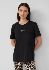 Schwarzes Baumwoll-T-Shirt mit Rundhalsausschnitt und kurzen Ärmeln, mit weißem Text: "DEIN KÖRPER IST DEIN WICHTIGSTES GUT" auf der Vorderseite.