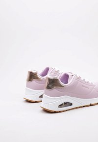 Sneakers atletici rosa con tomaia in tessuto texture, dettagli dorati metallici, suola intermedia bianca, ammortizzazione ad aria e suola esterna marrone chiaro.