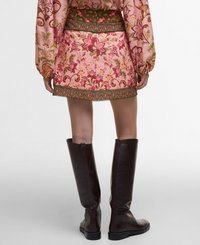 Jupe rose à motifs floraux avec une taille verte et une garniture décorative, associée à de hautes bottes en cuir marron au fini lisse.