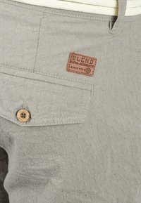 Pantalons gris clair avec un motif en tissu texturé, dotés d'un bouton de poche et d'une étiquette en cuir de marque intitulée "BLEND."