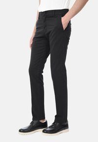 Pantaloni neri con un design slim fit, realizzati in tessuto intrecciato. Presentano tasche frontali, una chiusura con zip e una vita piatta. Abbinati a scarpe nere.